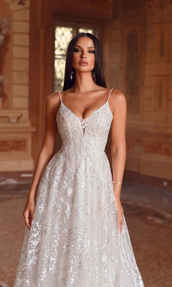 A woman in the Alyce 7121 long white dress stands indoors, with ornate walls and a large window behind her.